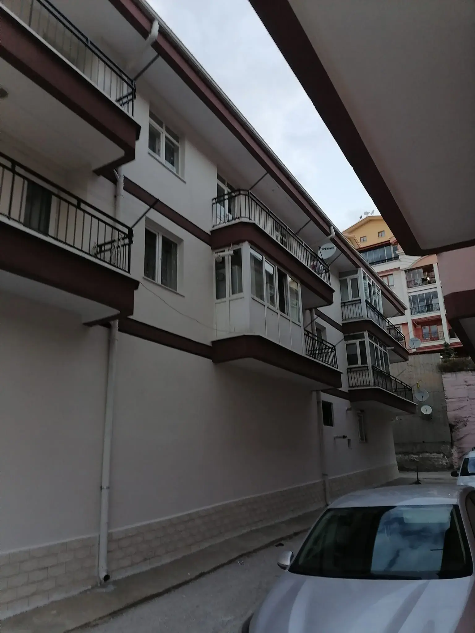 Üç katlı apartman: krem dış cephe, kahverengi kat silmeleri ve saçak altı, taş desenli subasman
