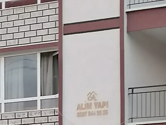 Cephede tuğla desenli paneller, taş şerit ve Alim Yapı levhası, yakın plan