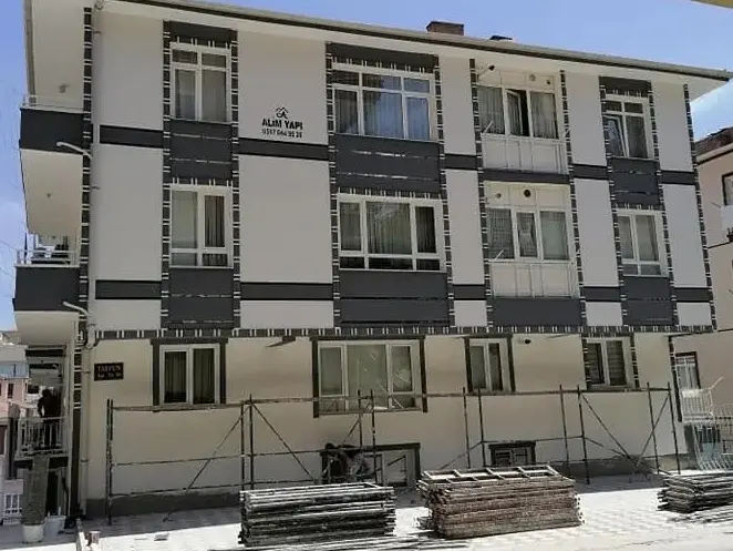 Dört katlı bina, beyaz cephe ve antrasit paneller, önde sökülmüş iskele parçaları
